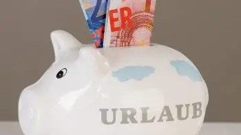 Auf dem Foto sieht man ein weisses Sparschwein wo der Begriff Urlaub draufsteht und in der Öffnung sind ein 20 euro schein und ein 10 euro Schein